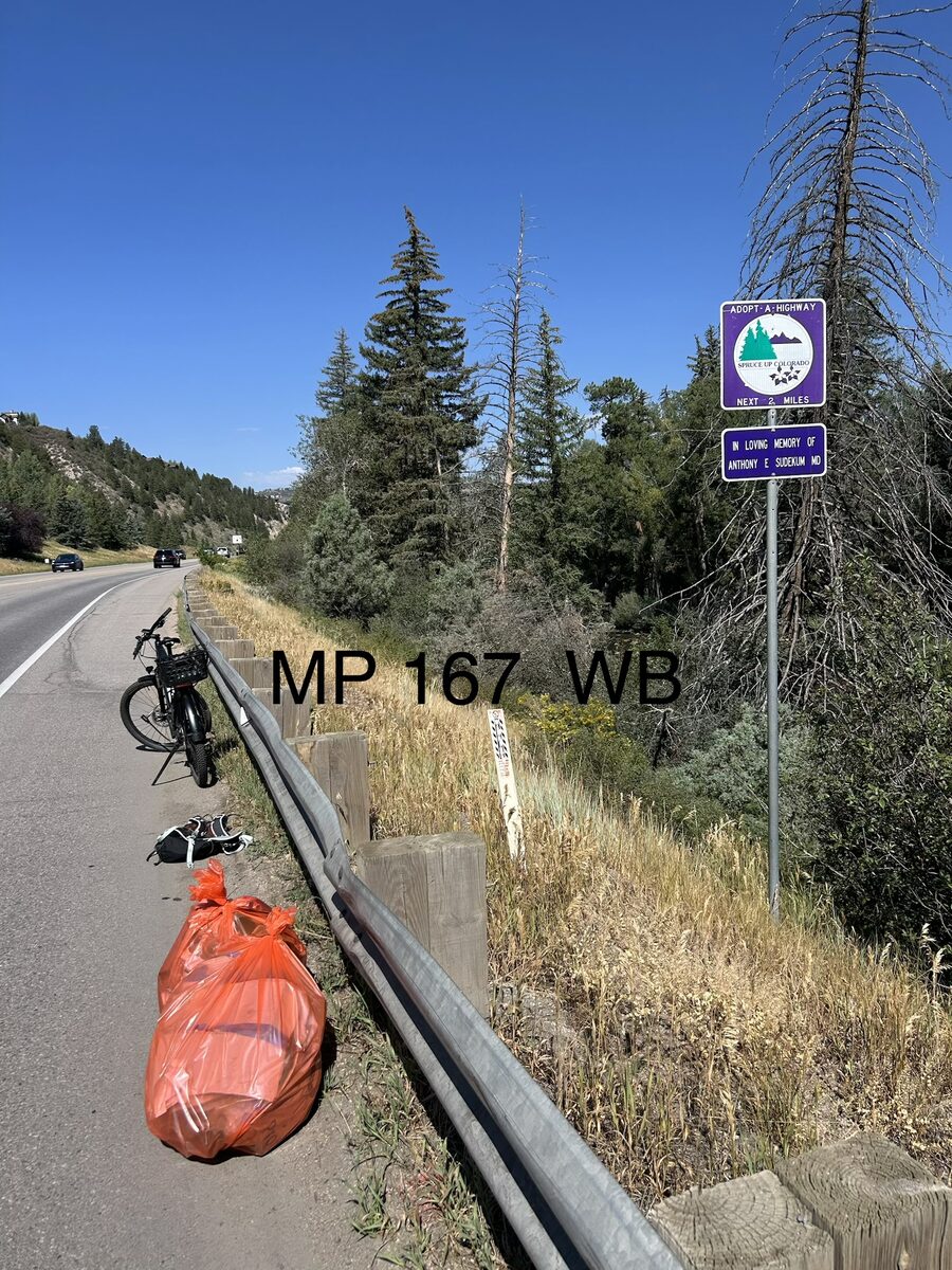 Adopt-a-Highway sign beside U.S. Highway 6 with Rick's bicycle and a filled orange cleanup bag nearby